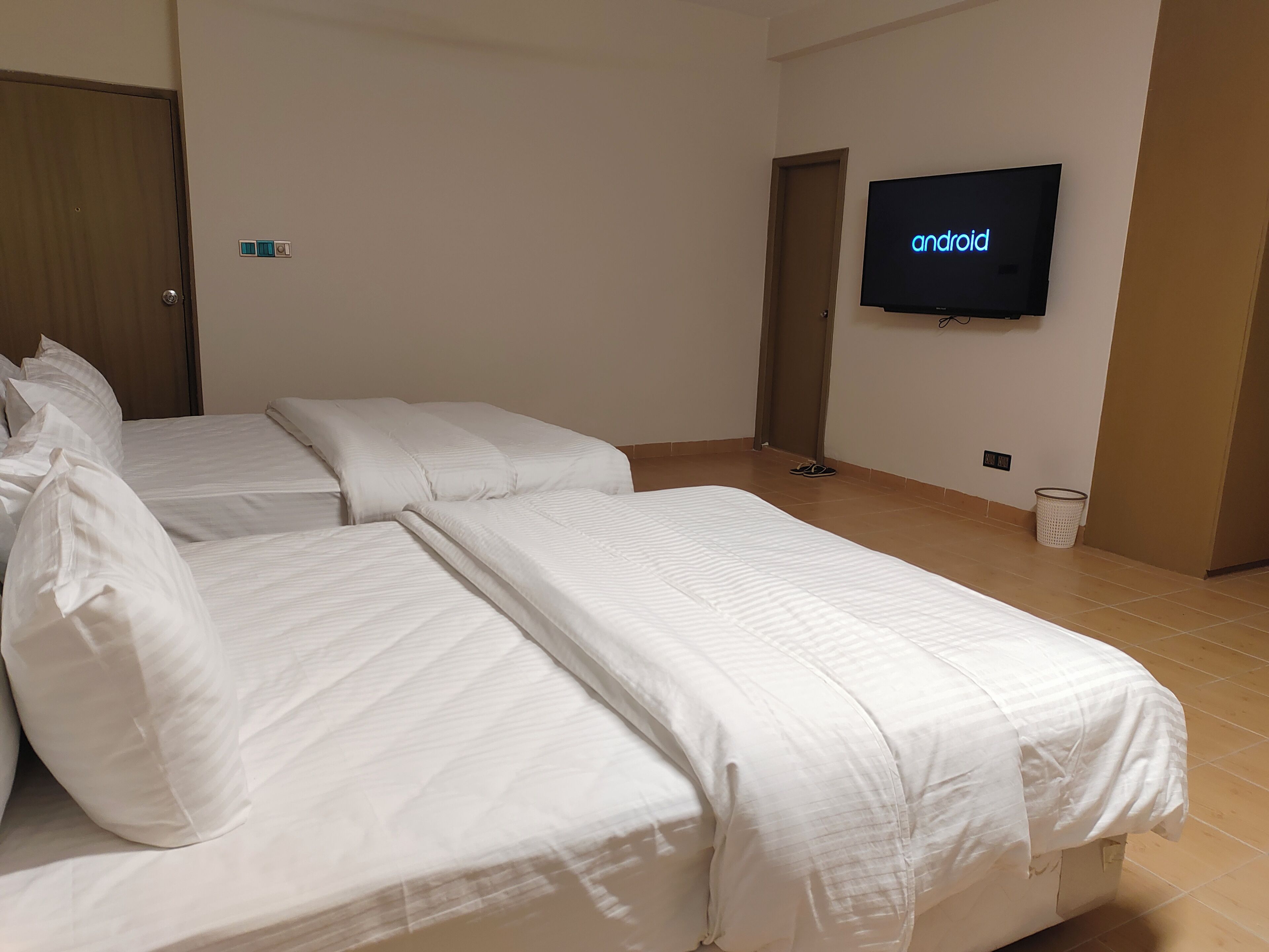 Una habitación de hotel con dos camas, un televisor montado en la pared y una puerta.