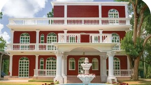 A two-story building with a central fountain, surrounded by a garden with flowers and a pool. - Kazi Resort & Hotel (Kapasia)