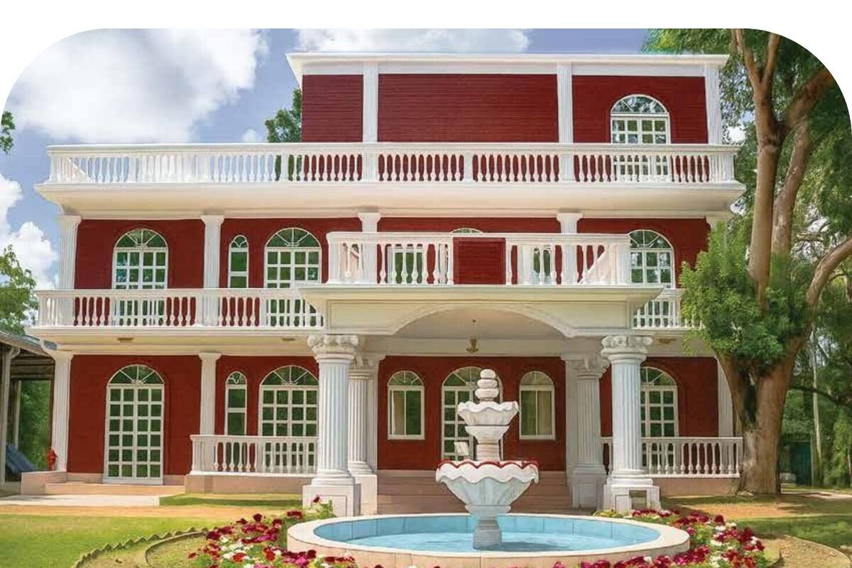 A two-story building with a central fountain, surrounded by a garden with flowers and a pool.