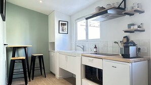 Une cuisine moderne avec des armoires blanches, un plan de travail en bois et un four encastré. On y trouve deux tabourets et une fenêtre au-dessus de l’évier.