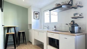 A modern kitchen with white cabinets, a wooden countertop, and a built-in oven. There are two stools and a window above the sink.