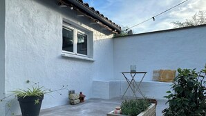 Une cour avec un mur blanc, une fenêtre, une table en bois et des plantes en pot.