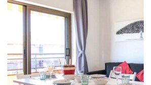 Un coin repas avec une table dressée pour deux personnes, une fenêtre avec des rideaux et une vue sur le balcon.