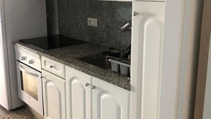 Une cuisine avec des meubles blancs, un plan de travail en granit, un four encastré et un évier en acier inoxydable.