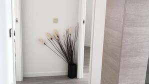 Un couloir avec une porte blanche, un vase noir contenant des plantes séchées et un interrupteur sur le mur.