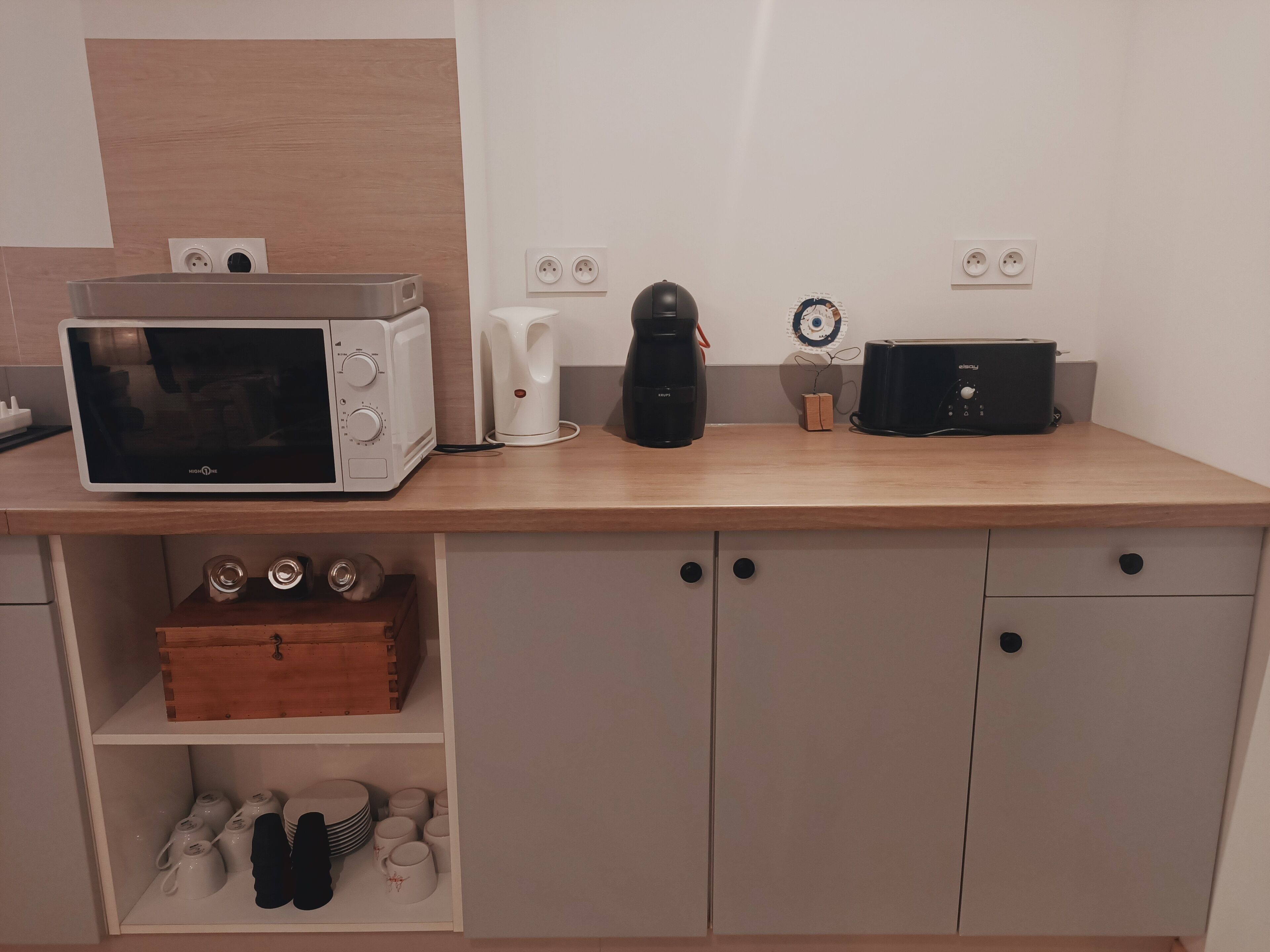 Ett litet kök med mikrovågsugn, kaffebryggare, brödrost och en liten trälåda på bänkskivan.