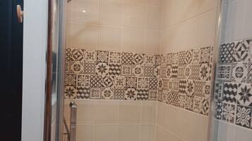 Une douche avec une porte en verre, un pommeau de douche à main et un mur recouvert de carreaux décoratifs.