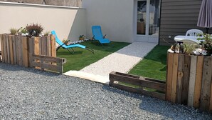 Ein Garten mit einem Kiesweg, zwei blauen Liegestühlen, einem Holzzaun und einer kleinen Gartenanlage mit Pflanzen und einem Vogelbad.