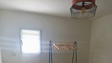 Un dormitorio con una cama litera, una silla de mimbre, un ventanal pequeño, un radiador y una lámpara colgante.