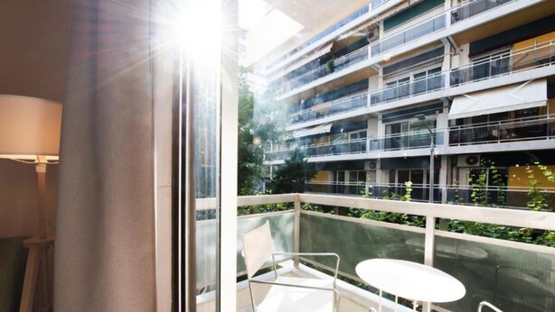 A balcony with a glass railing, a white chair, and a small round table. - Mandarin apartments by halu! (Thessaloniki)
