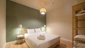 A neatly made bed with white linens and a rolled towel, a bedside lamp, and a wooden nightstand with a basket. - Mandarin apartments by halu! (Thessaloniki)