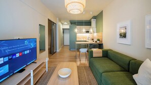 A modern living room with a flat-screen TV, a green sofa, a wooden coffee table, and a kitchen area in the background. - Mandarin apartments by halu! (Thessaloniki)
