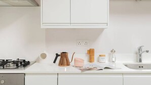 Una cocina moderna con armarios blancos, una estufa a gas, una cafetera, un hervidor, un salero, un molinillo de pimienta, un frasco de vidrio y un lavamanos con grifo.