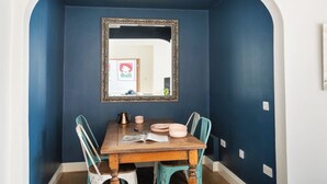 Un comedor con pared azul oscuro, una mesa de madera y dos sillas. Un espejo cuelga sobre la mesa.