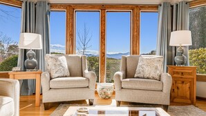 A living room with two armchairs, a coffee table, and a view of mountains through large windows. - Daisy Farm | Pool, Hot Tub & Animals 🐴 + Biltmore Pass Near Asheville (Candler)