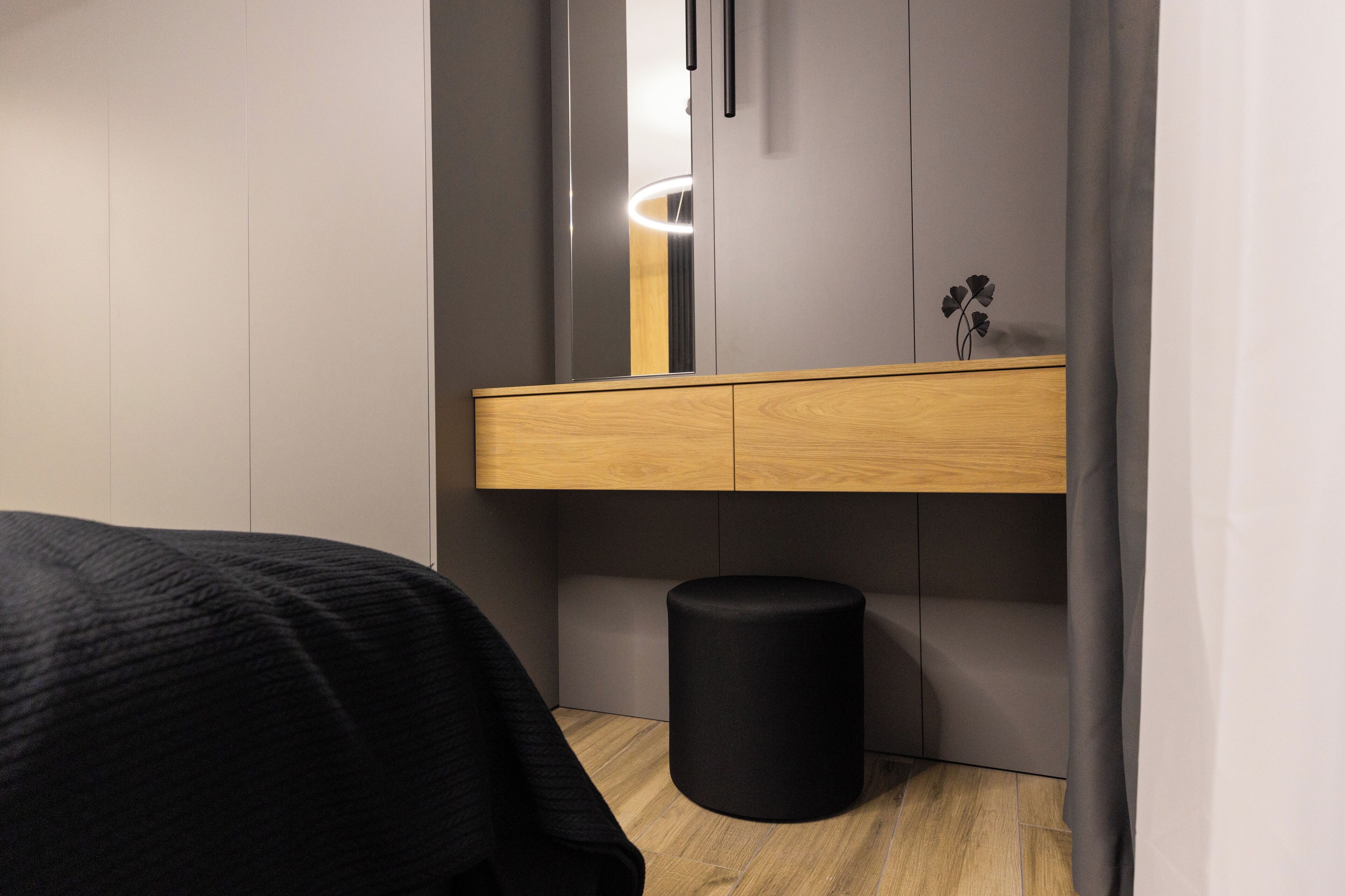 A modern bedroom with a wooden bed, a bedside table, a mirror, and a black cylindrical object on the floor.