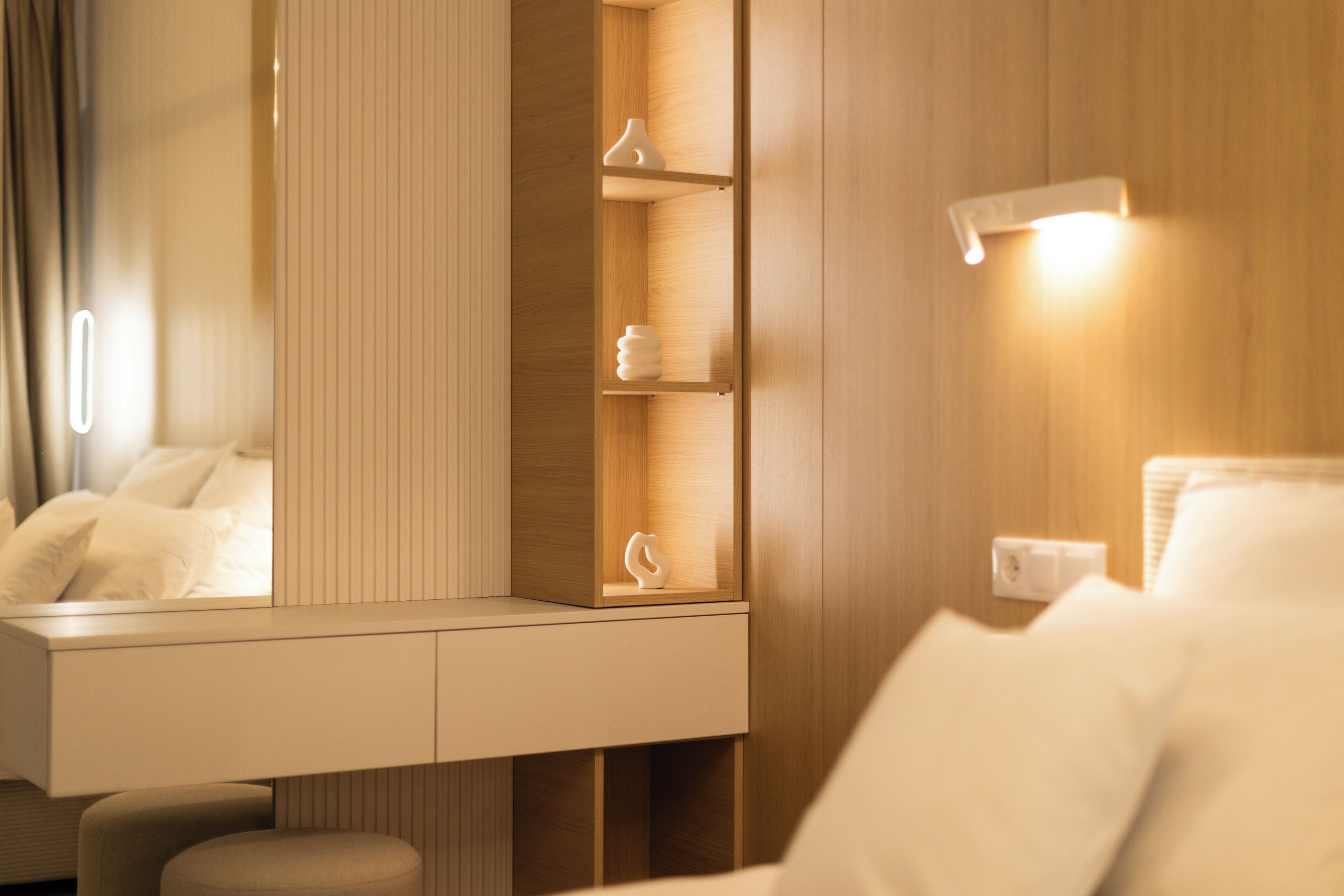 A modern hotel room with a wooden vanity, a mirror, and a bedside table.