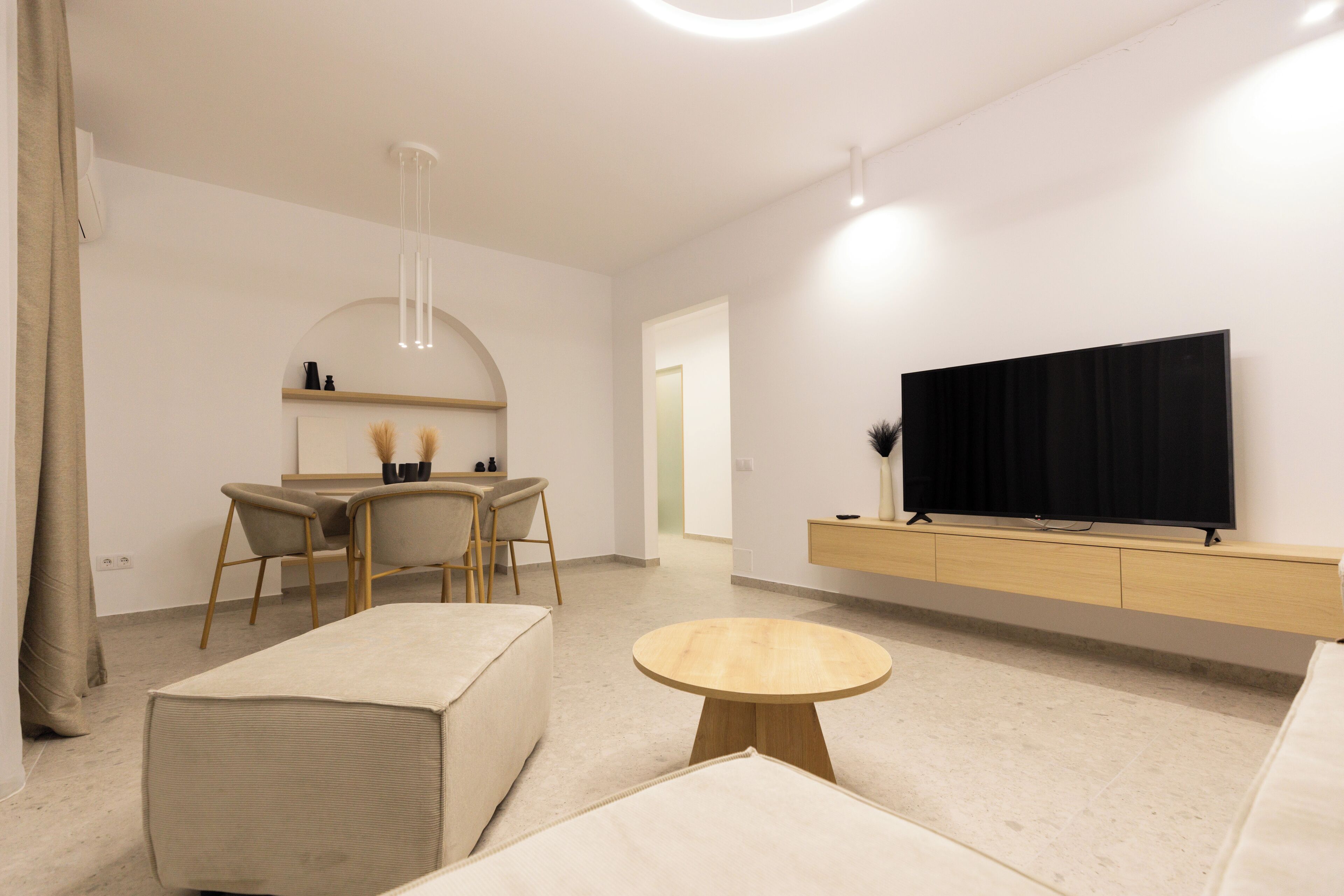 A modern living room with a sofa, a round coffee table, a TV on a wooden stand, and a dining area with chairs and a table.