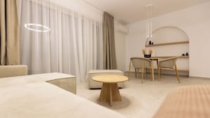 Una habitación de hotel moderna con una mesa redonda de madera, un sofá, una silla y un escritorio pequeño con una lámpara.