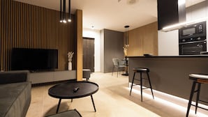 Una sala de estar moderna con televisor, sofá y mesa de centro. Hay una zona de cocina con microondas y un taburete de bar.