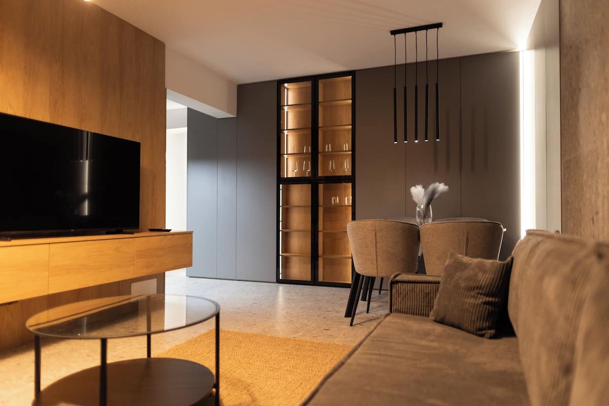A modern living room with a flat-screen TV, a glass coffee table, a sofa, and a bookshelf.