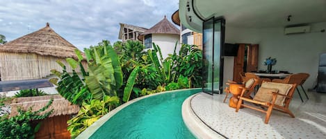A modern villa with a swimming pool, lush tropical plants, and a dining area with wicker furniture.