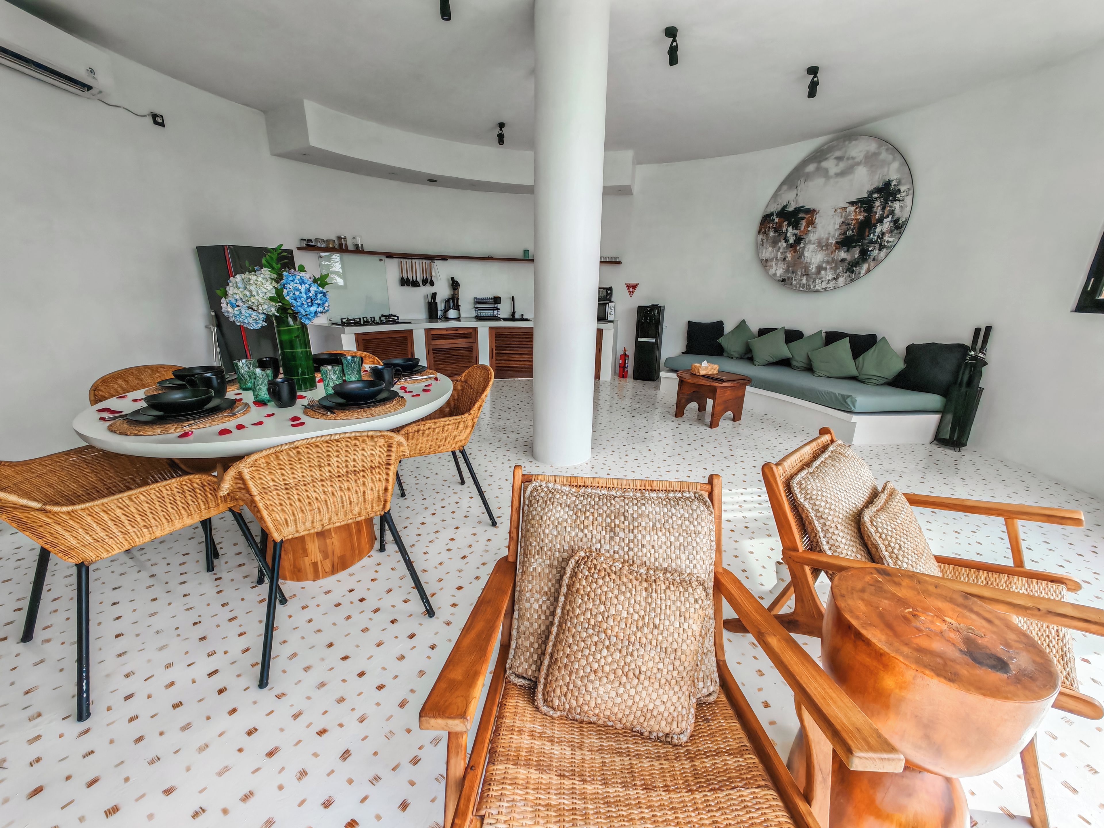 A modern living space with a dining area, a sofa, and a kitchen in the background.