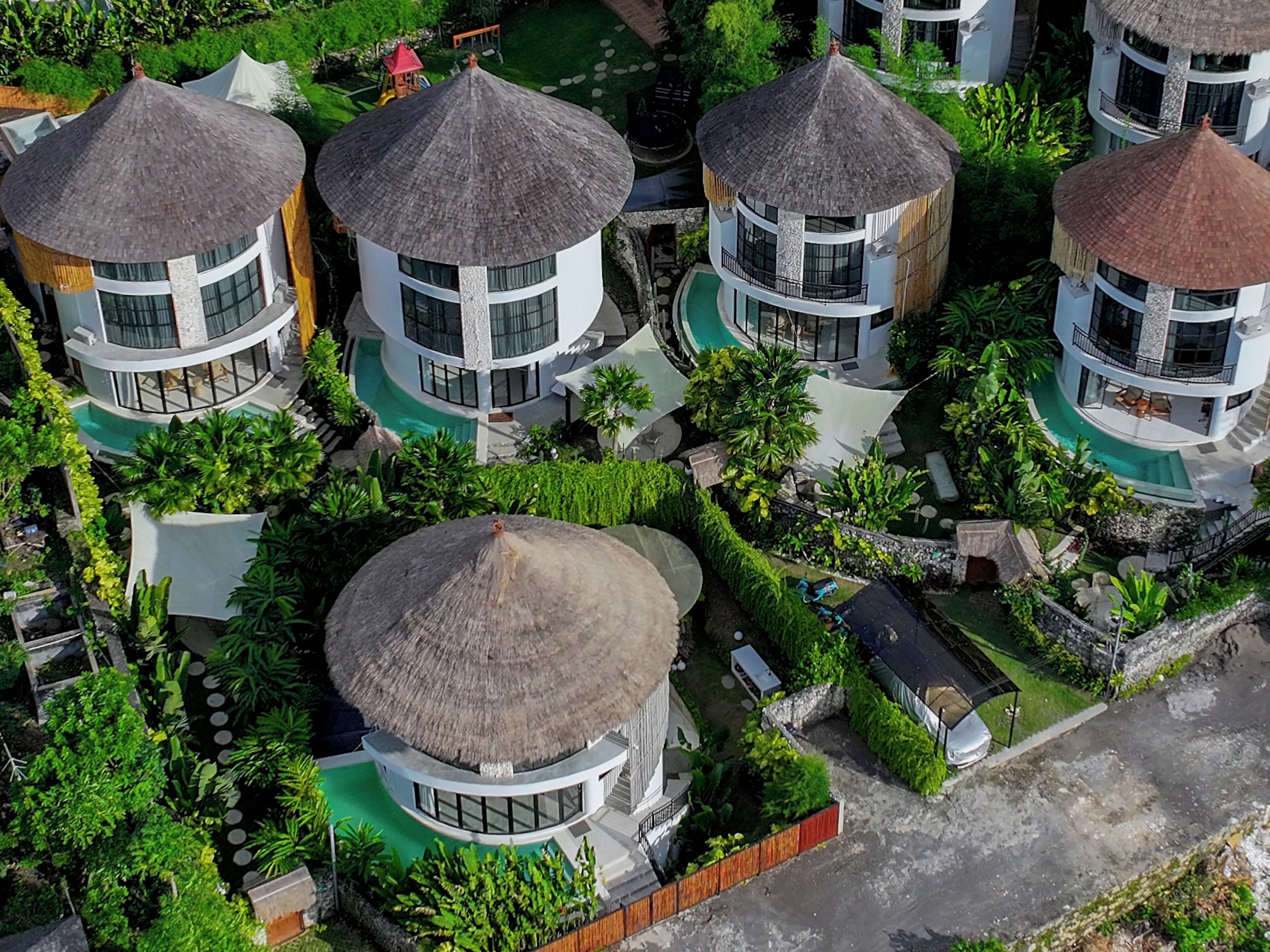 A cluster of circular buildings with thatched roofs, surrounded by lush greenery and a swimming pool.