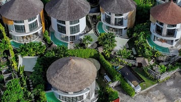 A cluster of circular buildings with thatched roofs, surrounded by lush greenery and a swimming pool.