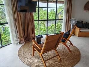 A room with a large window, a television, a fan, and wicker furniture. - Hillstone Luxury Village (Ungasan)