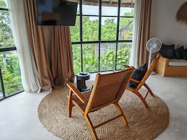 A room with a large window, a television, a fan, and wicker furniture.
