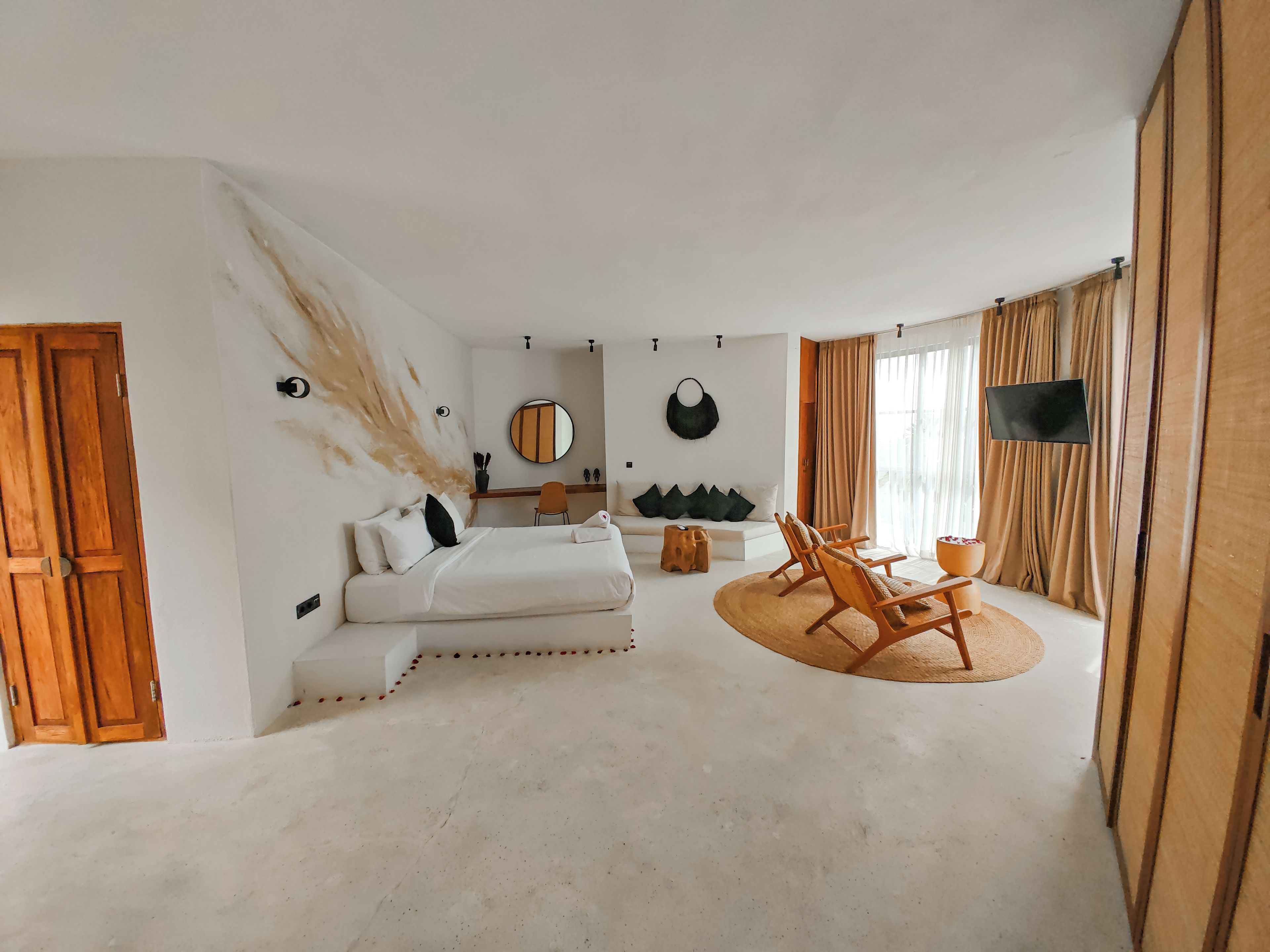 Une chambre moderne avec un grand lit, un coin salon avec un fauteuil, une télévision et une grande fenêtre avec des rideaux.