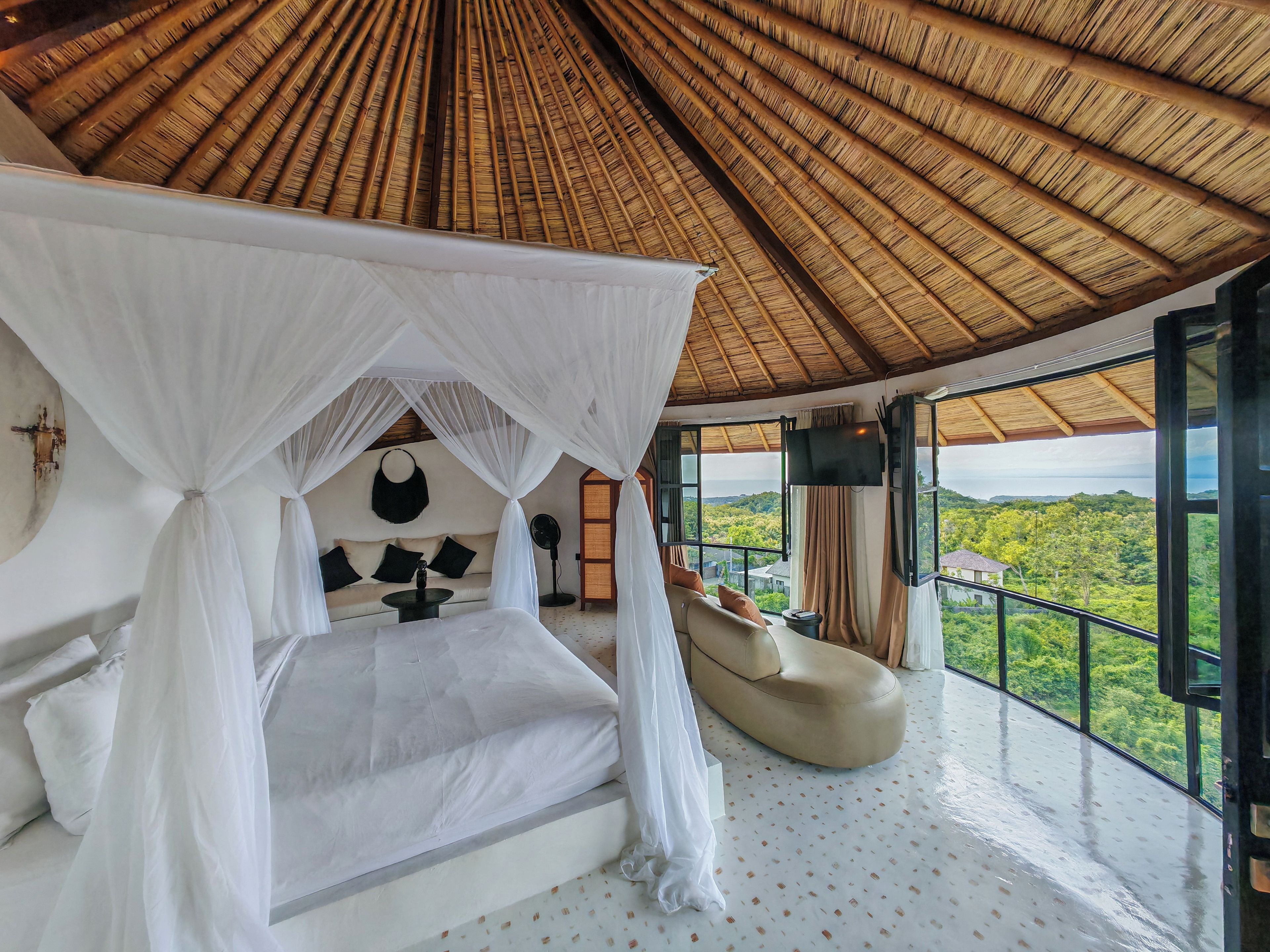 A bedroom with a canopy bed, a sofa, a TV, and a view of the landscape.
