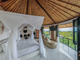 A bedroom with a canopy bed, a sofa, a TV, and a view of the landscape.