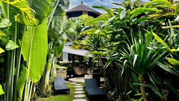 Un exuberante jardín con un sendero que lleva a un espacio de descanso con sillones de sala.