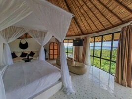 Una habitación con cama bajo un dosel, un sofá, un televisor y vista al paisaje.