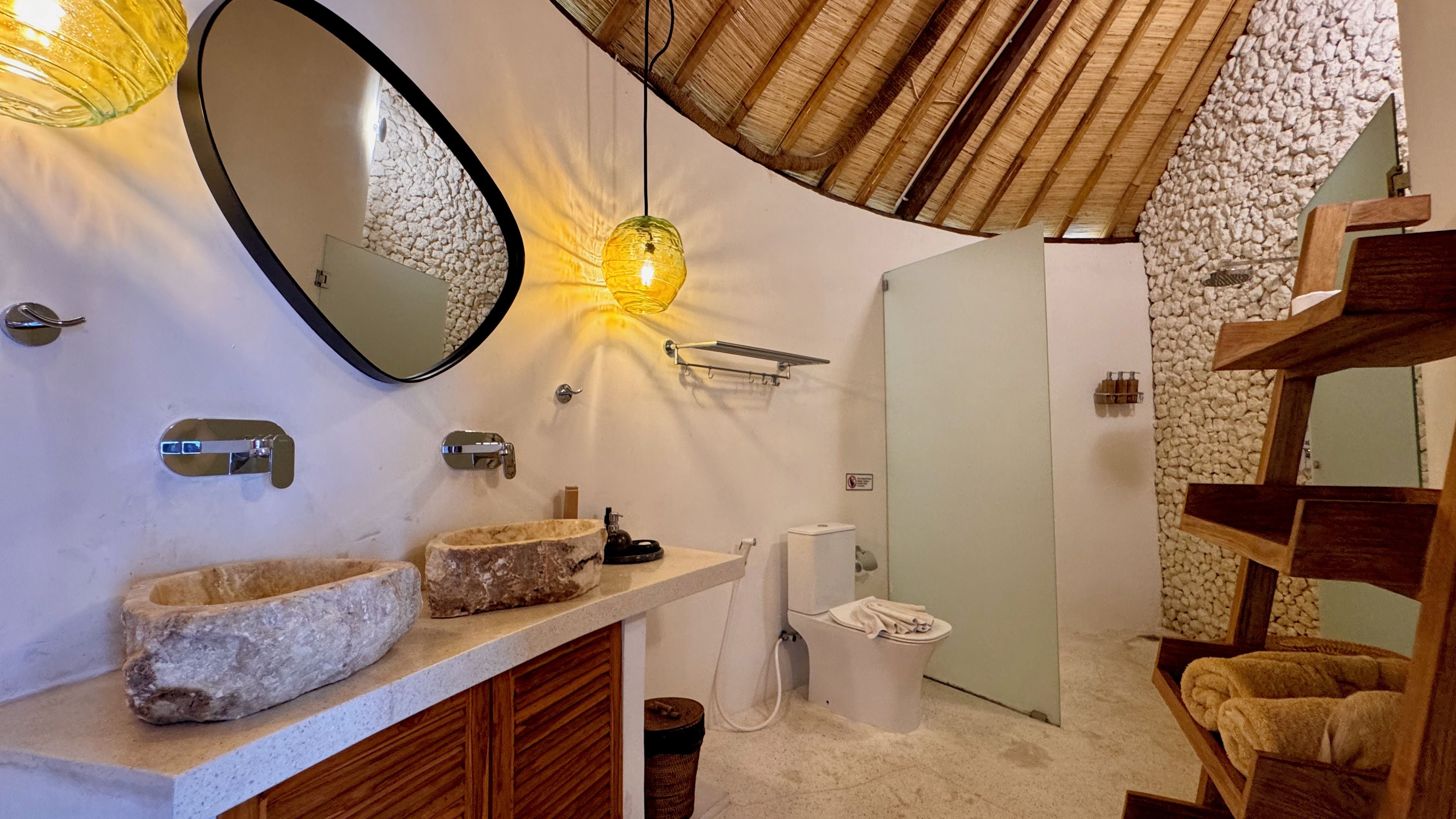 A bathroom with a stone sink, a mirror, a towel rack, and a wooden shelf.