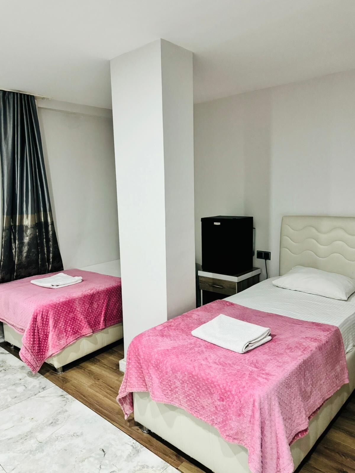 Two single beds with pink towels, a TV on a nightstand, and a white headboard.
