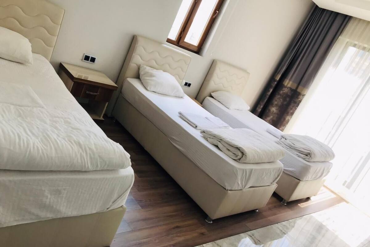 A hotel room with two beds, a nightstand, a window, and a view of the outdoors.