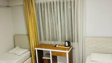Una habitación pequeña y limpia con dos camas individuales, un escritorio de madera con hervidor y una cortina.