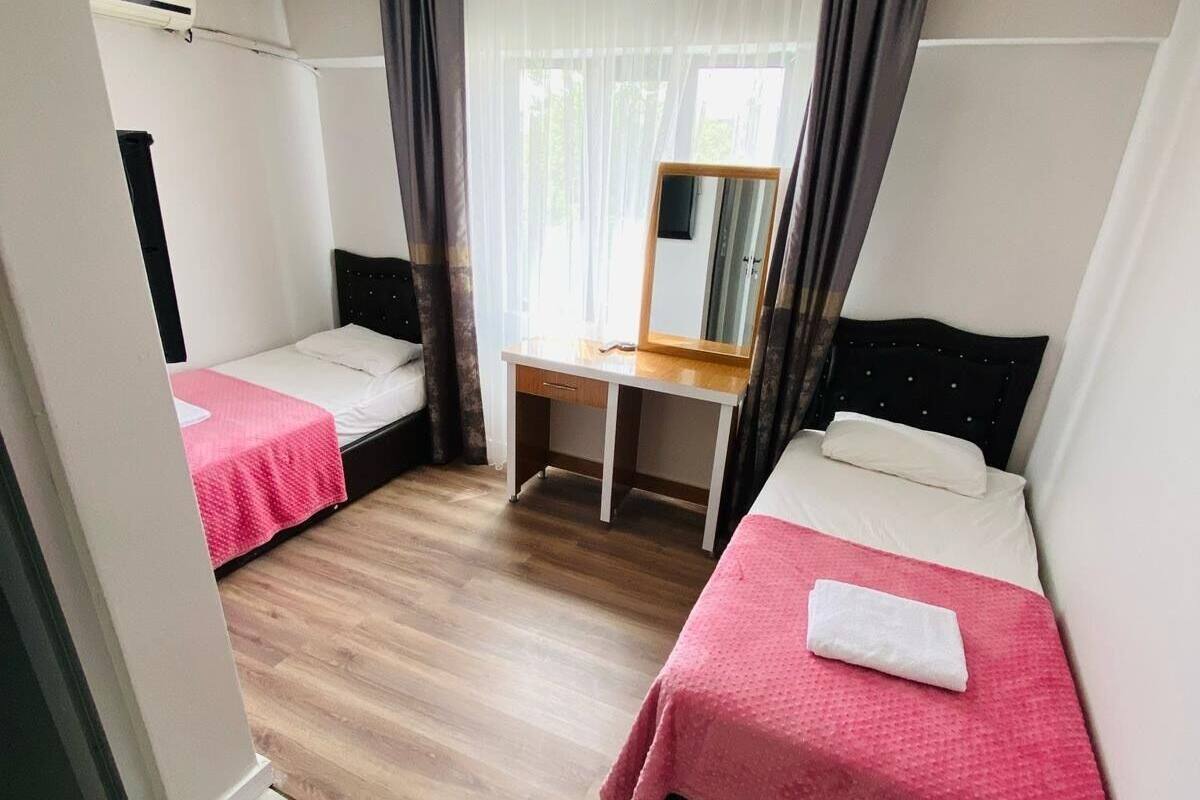 A small, modern room with two single beds, a desk, and a mirror.