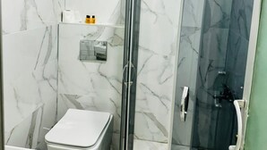 A bathroom with a toilet, a shower enclosure, and a marble-tiled wall. - Dara Otel Midyat (Midyat)