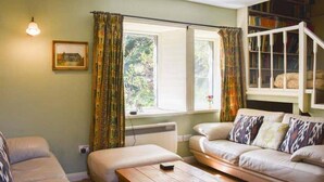 A cozy living room with a sofa, a wooden coffee table, and a bookshelf filled with books. - Red Squirrel Haven 2BR House - Sleeps 4 - Parking (Hawes)