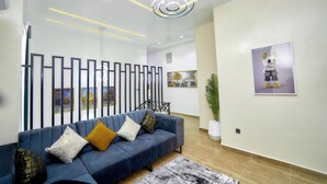 A modern living room with a blue sofa, decorative pillows, a contemporary light fixture, and artwork on the walls.