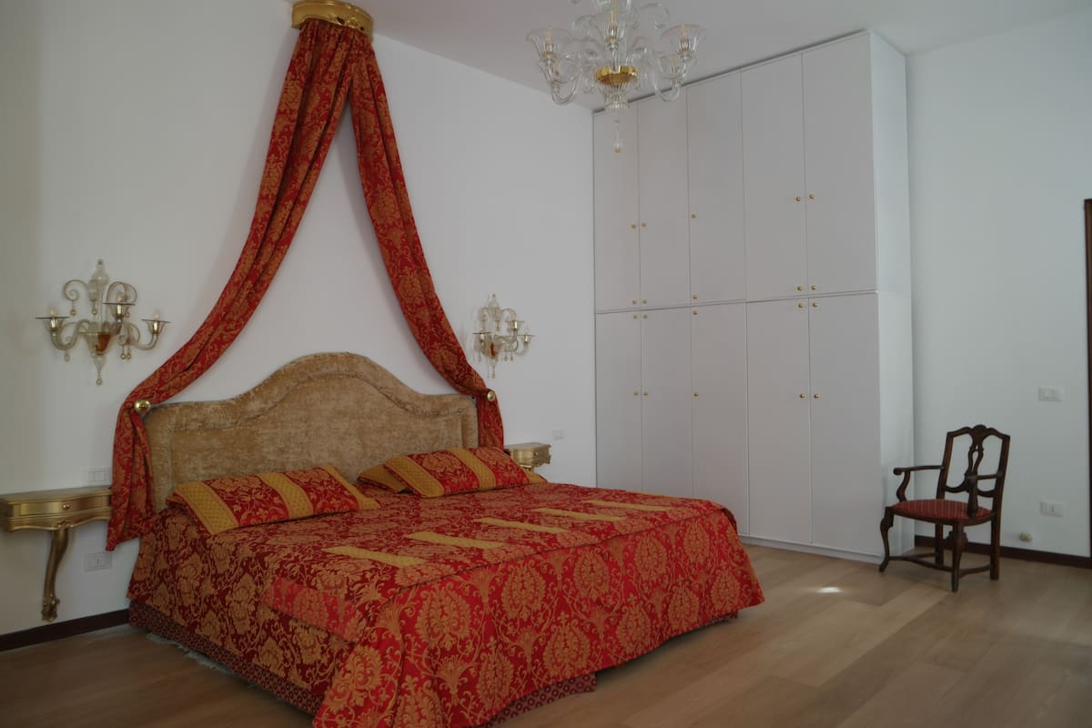 A bedroom with a four-poster bed, a chandelier, a wardrobe, and a chair.