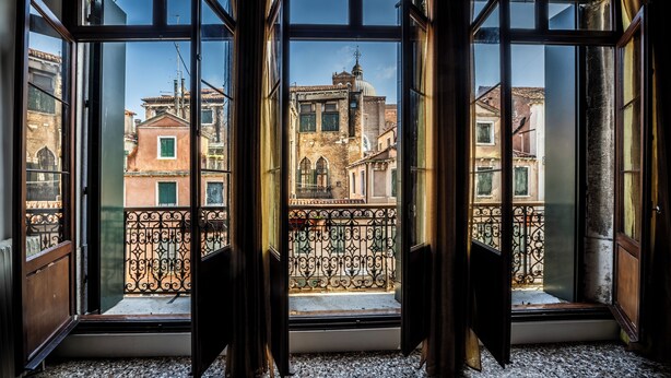 A room with large windows, a balcony with wrought iron railing, and a view of historic buildings. - Savoia & Jolanda Apartments  (Venice)