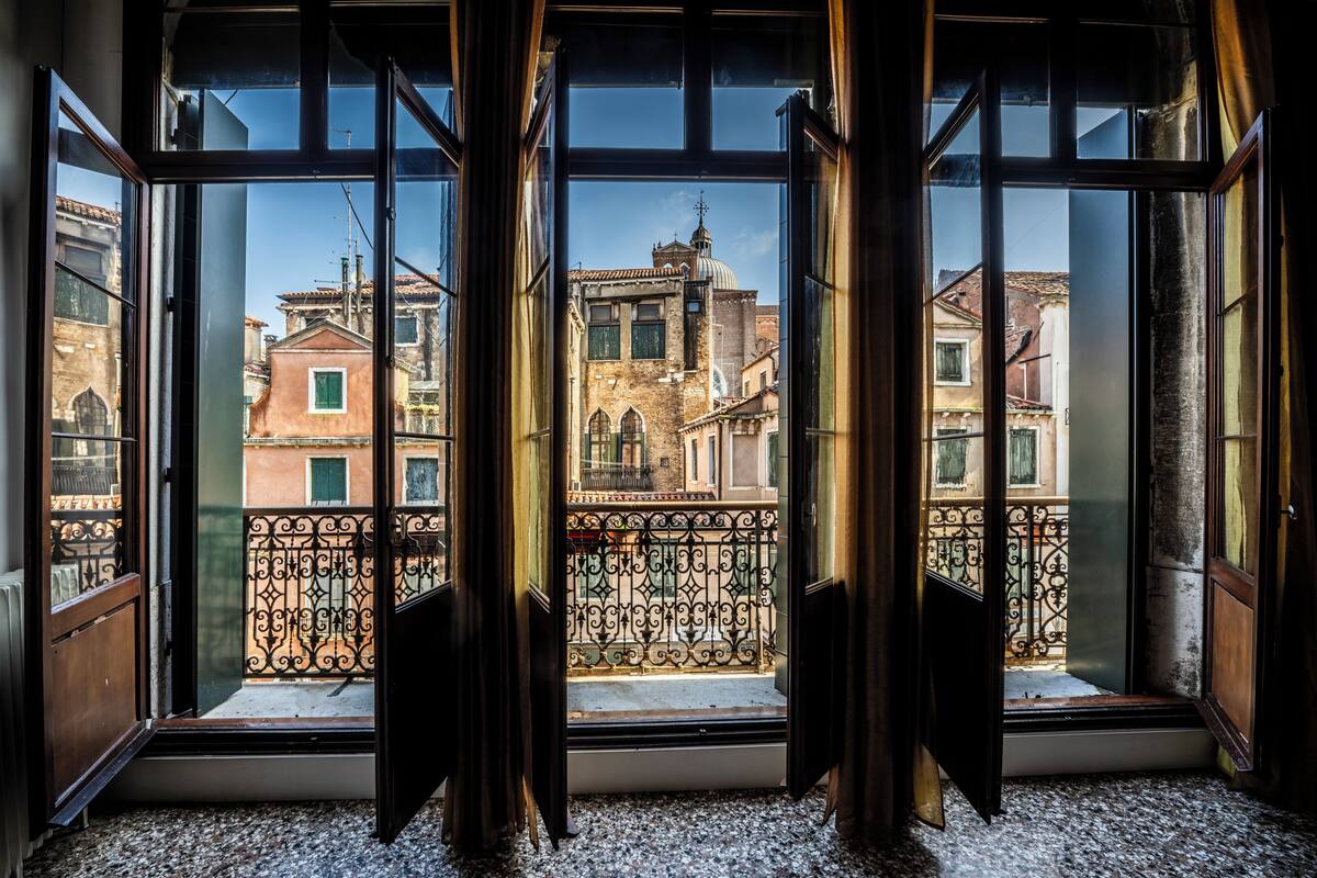 A room with large windows, a balcony with wrought iron railing, and a view of historic buildings.