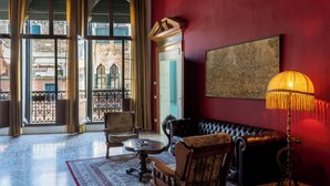 A room with a red wall, a black leather sofa, a wooden chair, a small round table, and a floor lamp. - Savoia & Jolanda Apartments  (Venice)