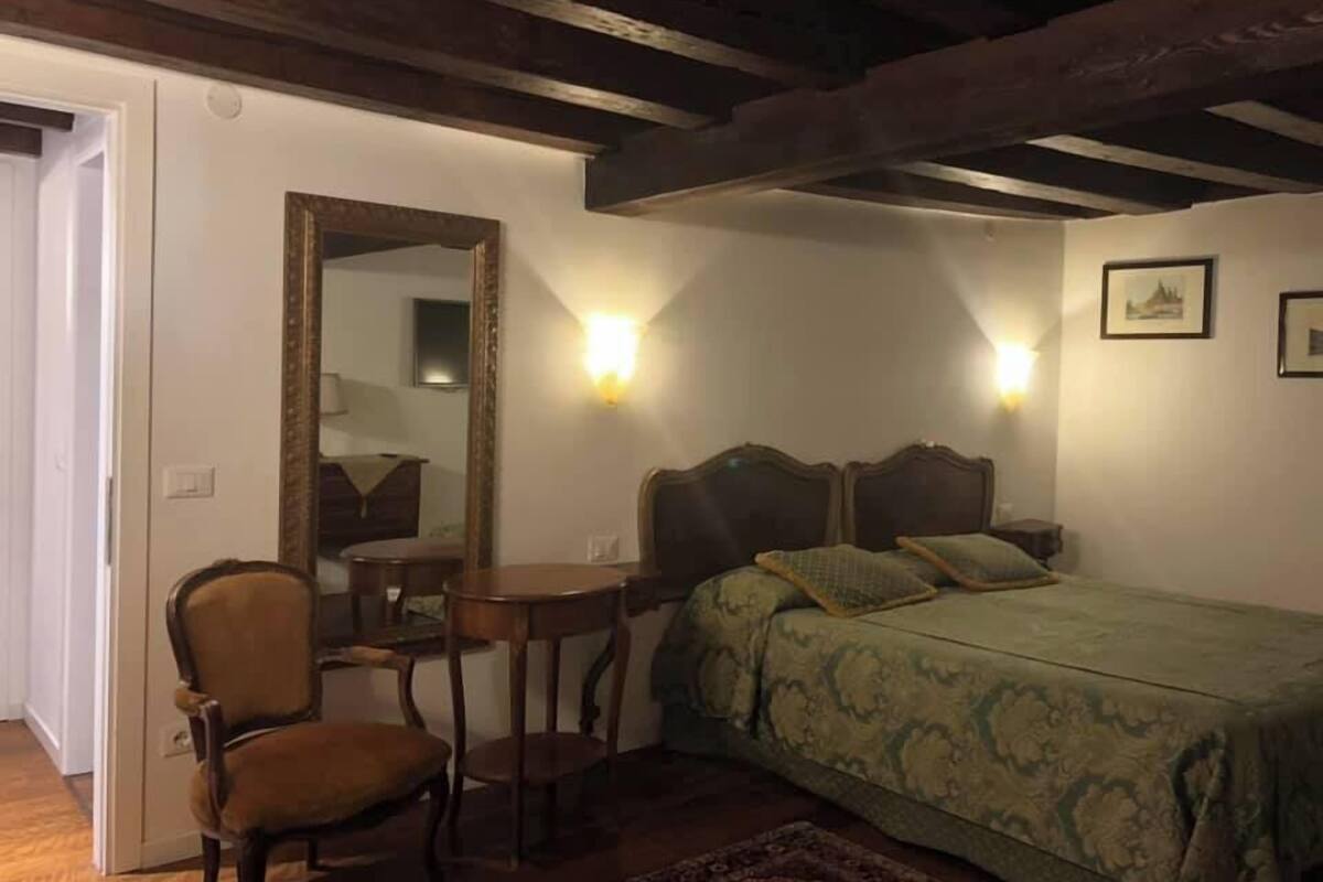 A bedroom with a bed, a chair, a table, and a mirror.