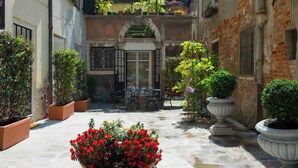 A courtyard with a table and chairs, potted plants, and a brick building. - Savoia & Jolanda Apartments  (Venice)